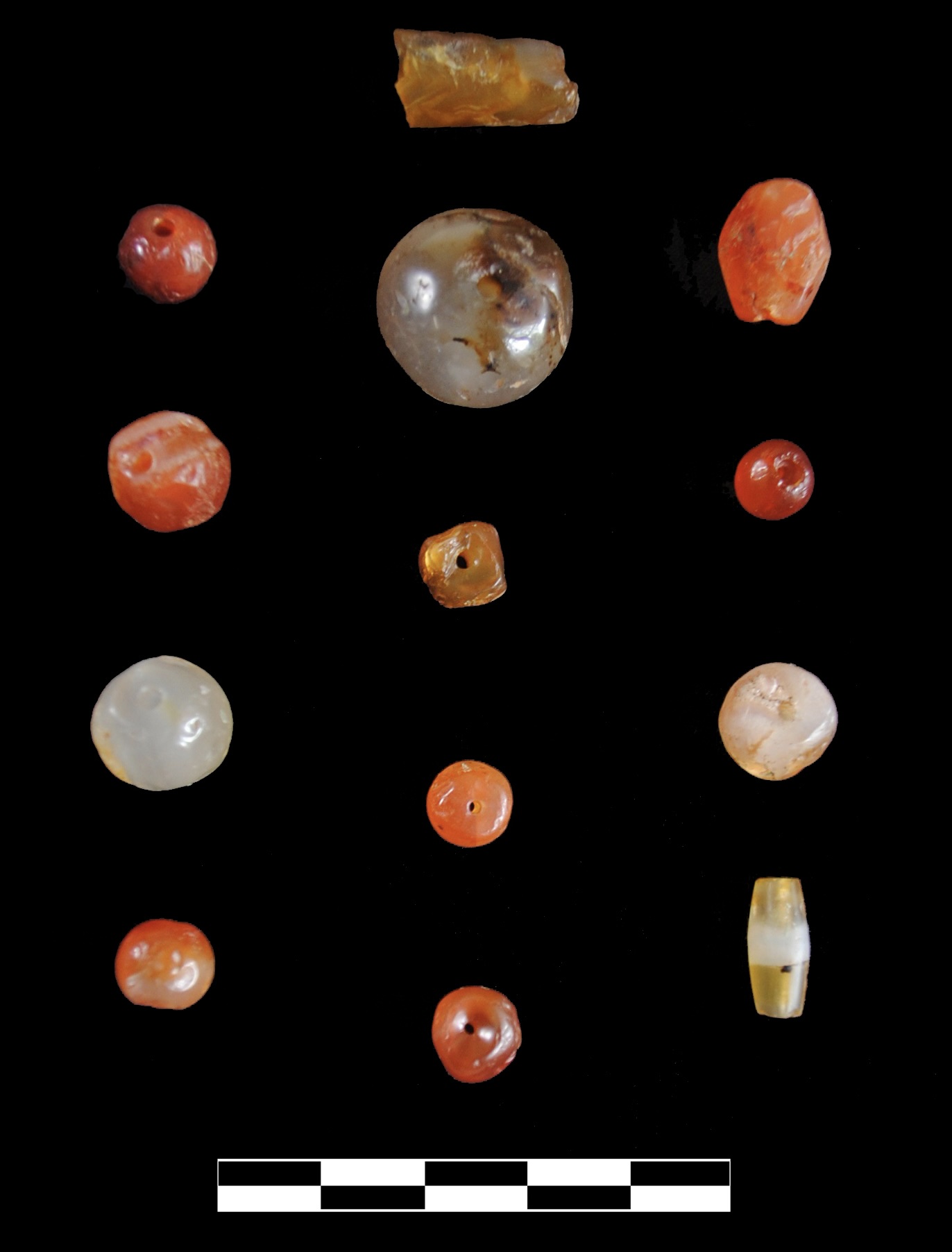 Carnelian beads on a black background with a cm scale bar at bottom